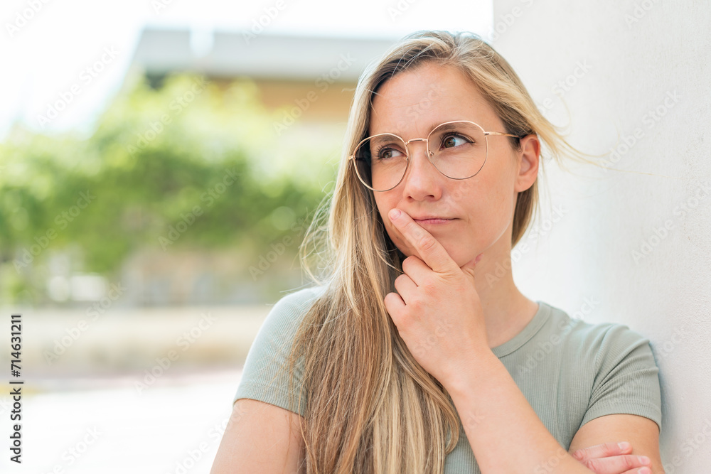 Young blonde woman at outdoors With glasses and having doubts Young blonde woman at outdoors With glasses and having doubts