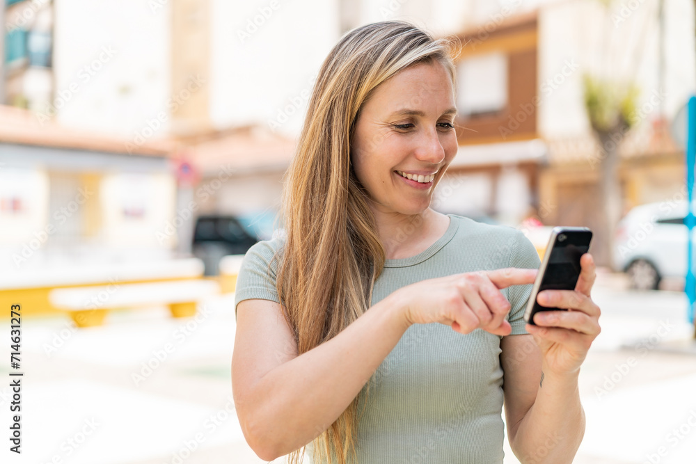 Young blonde woman at outdoors sending a message or email with the mobile Young blonde woman at outdoors sending a message or email with the mobile