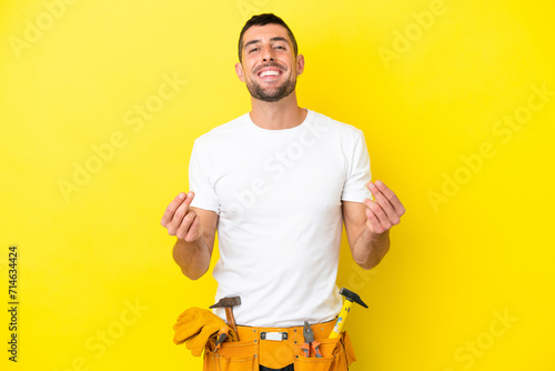 young electrician caucasian man isolated on yellow background making money gesture photo