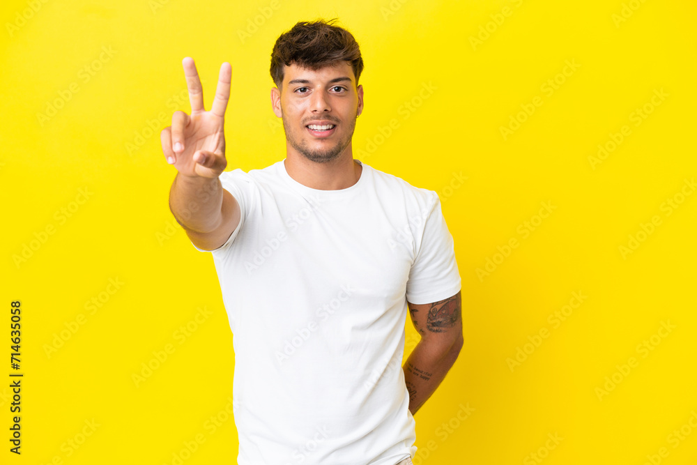 Young caucasian handsome man isolated on yellow background smiling and showing victory sign Young caucasian handsome man isolated on yellow background smiling and showing victory sign