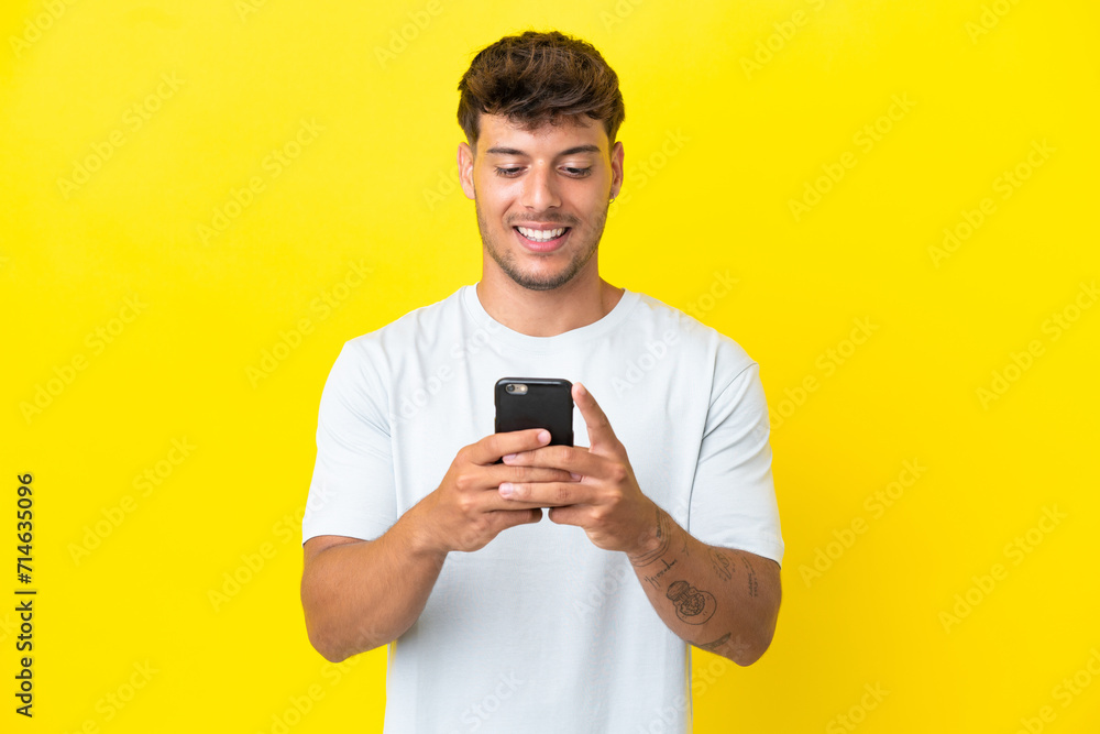 Young caucasian handsome man isolated on yellow background sending a message or email with the mobile Young caucasian handsome man isolated on yellow background sending a message or email with the mobile
