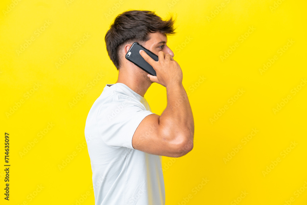 Young caucasian handsome man isolated on yellow background keeping a conversation with the mobile phone with someone Young caucasian handsome man isolated on yellow background keeping a conversation with the mobile phone with someone