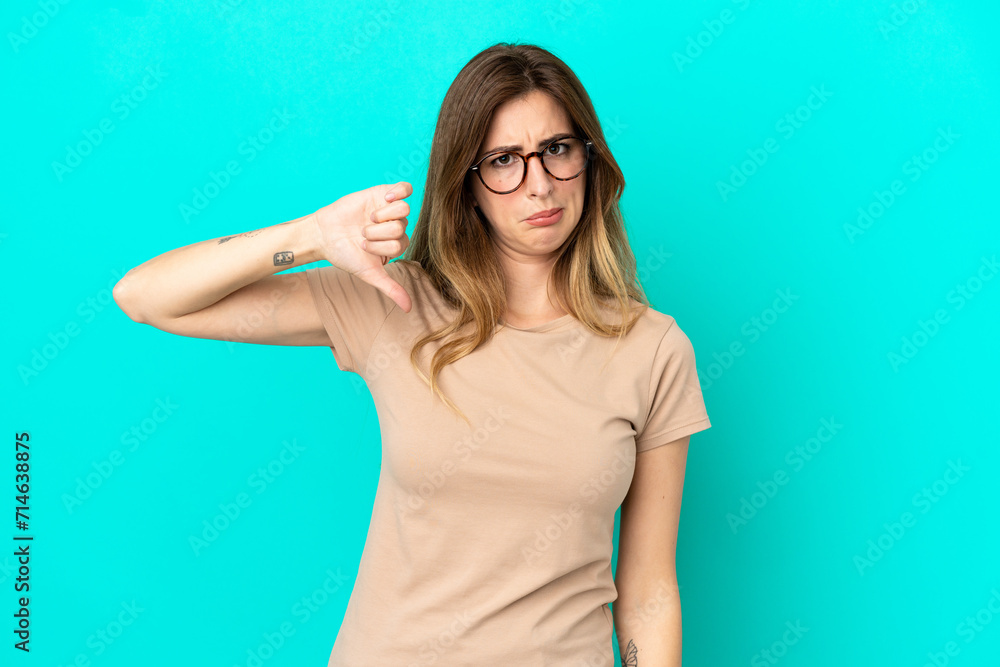 Young caucasian woman isolated on blue background showing thumb down with negative expression Young caucasian woman isolated on blue background showing thumb down with negative expression