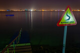 A slipery area danger sign in front of the bay, at night, with a staircase going down into the sea in the bay of Doha, qatar