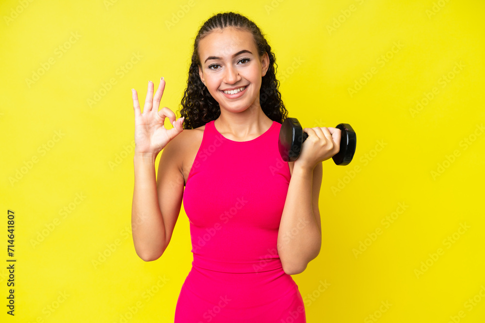 Young sport woman making weightlifting isolated on yellow background showing ok sign with fingers Young sport woman making weightlifting isolated on yellow background showing ok sign with fingers