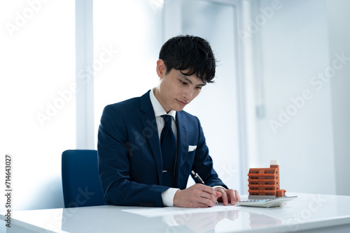 マンション模型を机に置き書類にペンで記入する男性 photo