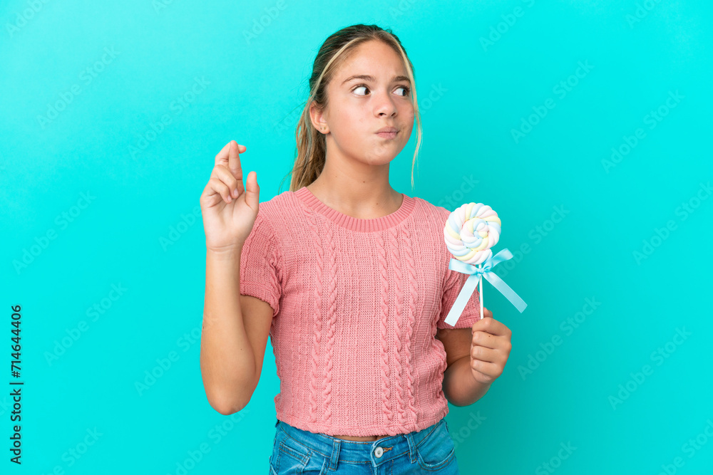 Little Caucasian girl holding a lollipop isolated on blue background with fingers crossing and wishing the best Little Caucasian girl holding a lollipop isolated on blue background with fingers crossing and wishing the best