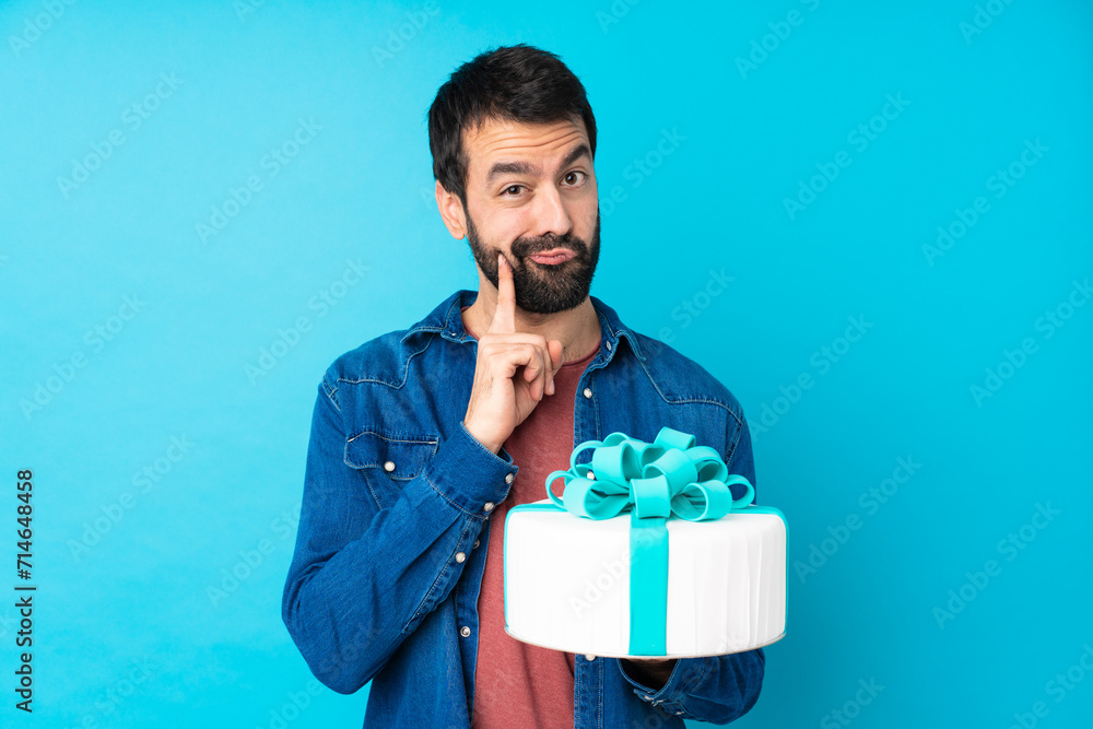 Young handsome man with a big cake over isolated blue background and looking front Young handsome man with a big cake over isolated blue background and looking front