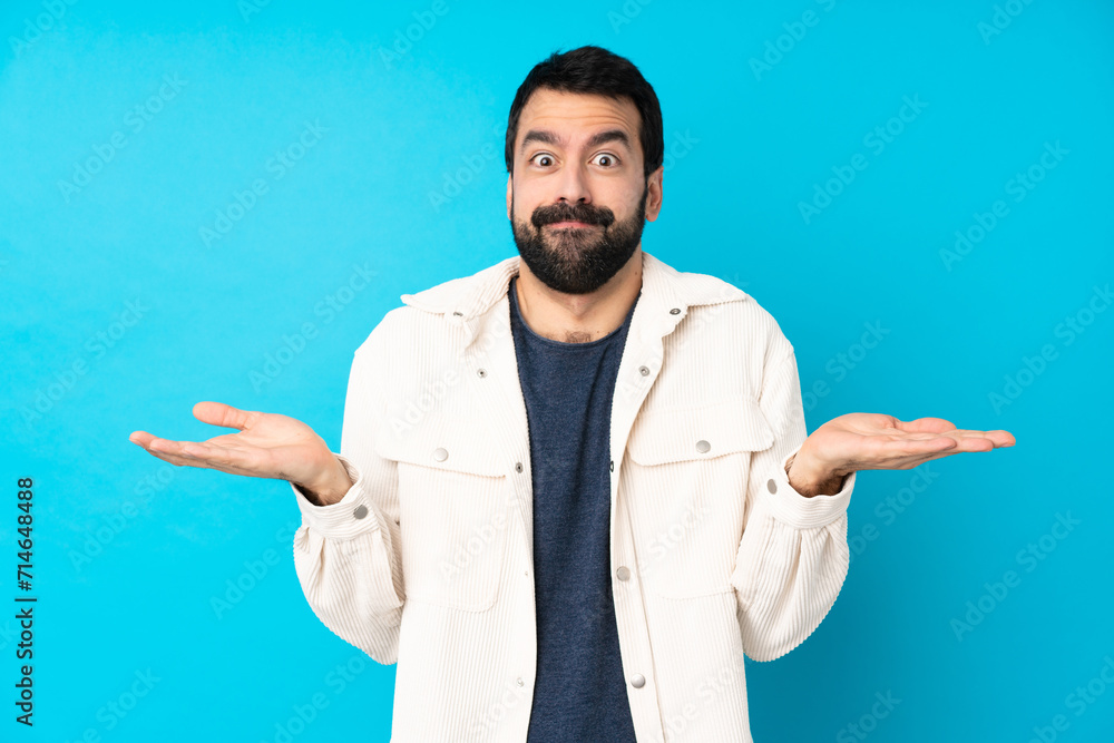 Young handsome man with white corduroy jacket over isolated blue background having doubts while raising hands Young handsome man with white corduroy jacket over isolated blue background having doubts while raising hands