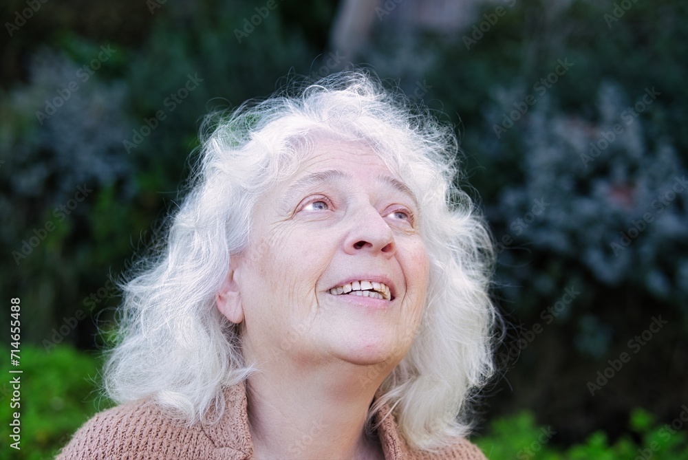 Portrait of a smiling gray-haired curly woman, looking up.