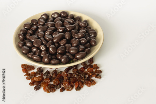 Dried raisins with dark chocolate in a bowl on a light gray background