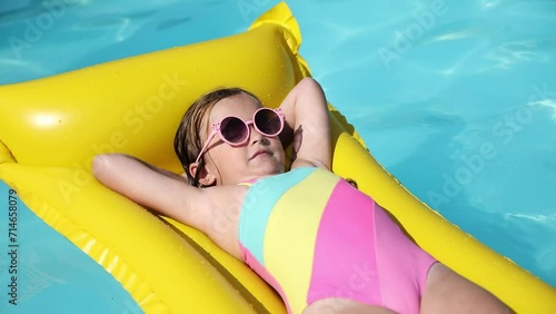 Cute little girl lying on inflatable mattress in swimming pool with blue water on warm summer day on tropical vacations. Summertime activities concept. Cute little girl sunbathing on air mattress photo