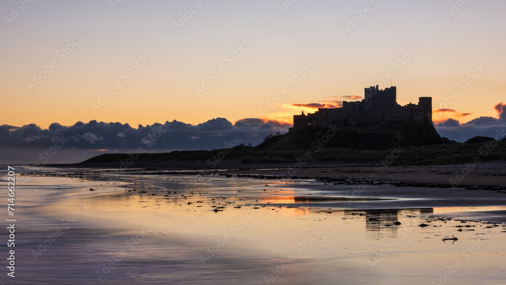 Beautiful landscape image of Northumberland beach in Northern England during Winter dawn with deep orange sky