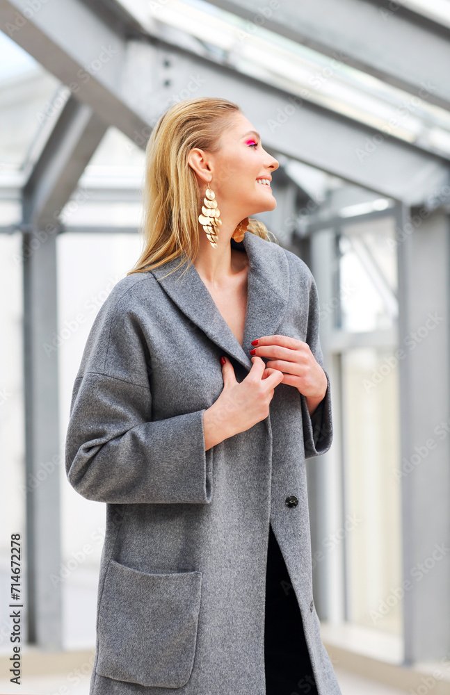 Fashion portrait of young elegant woman in Grey coat, black pants, black ankle boots and gold earrings Fashion portrait of young elegant woman in Grey coat, black pants, black ankle boots and gold earrings