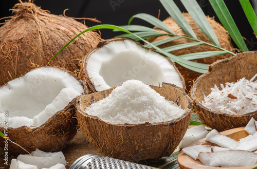 Fresh opened coconuts along with coconut slices, flakes and coconut leaves on a wooden table.