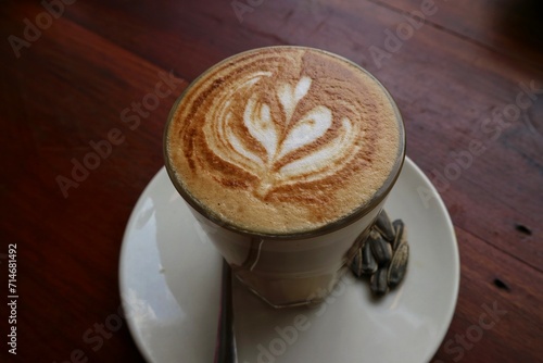 Coffee on wooden tabble. A cup of cappuccino with latte art with love art on the top surface. Fresh morning coffee with delicious milk foam on the cafe. clomplemented with Kwaci or Sunflower seeds.