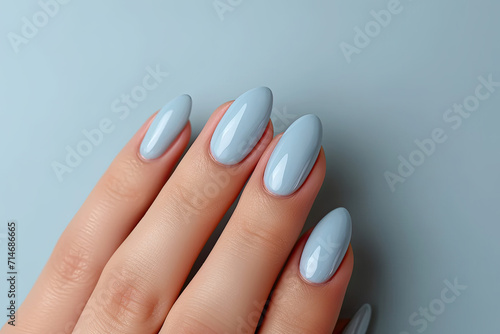  Close-up of woman fingers with beautiful blue manicure. Pastel color nail manicure with gel polish at luxury beauty salon. 