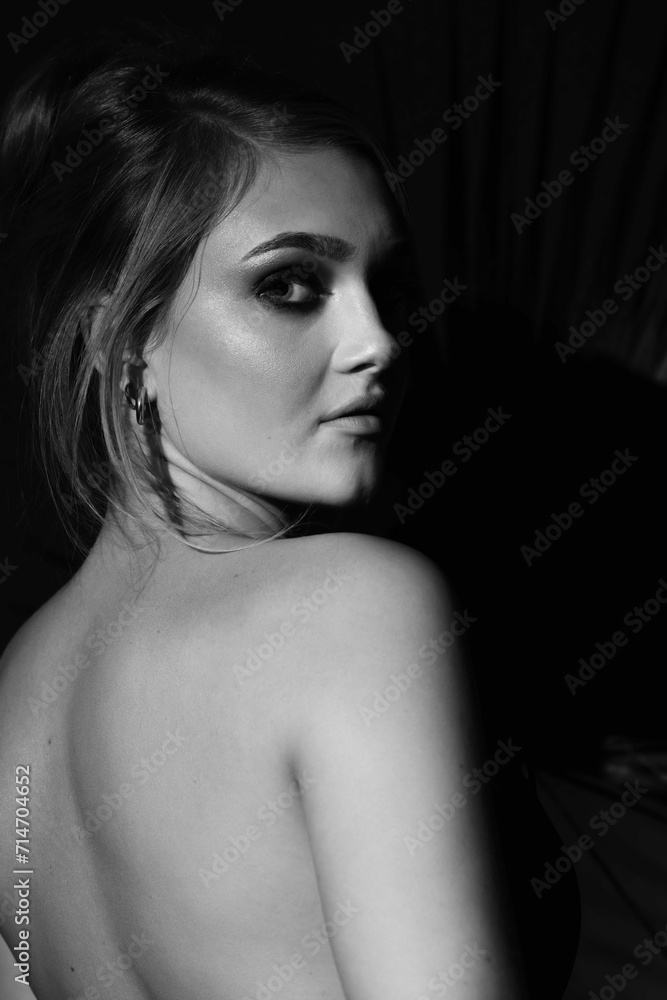 Naklejka premium Beauty, make-up and fashion concept. Beautiful woman with naked back studio portrait. Model looking to camera with seductive look and illuminated with studio light. Black and white image