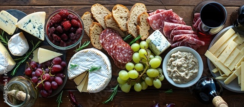 Assorted cheeses, fruits, meats, bread, dips on wooden table. Complements wine.