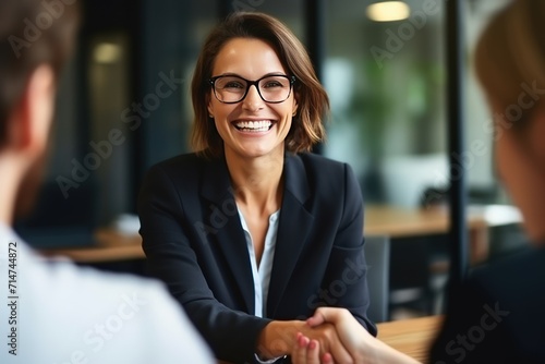 Middle aged Caucasian businesswoman in eyeglasses handshaking at office meeting. Cheerful female HR hiring recruit at job interview, bank or insurance agent. Lawyer making contract deal with client.
