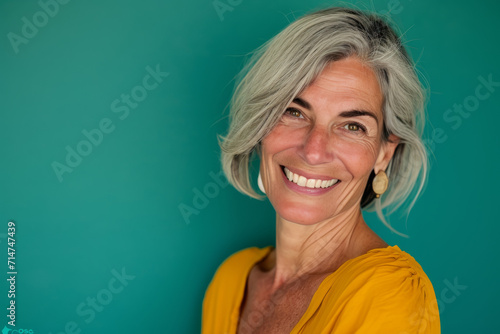 A woman with gray hair is smiling and wearing a yellow shirt