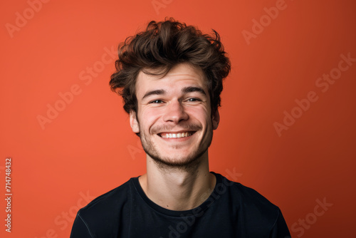A man with a beard is smiling in front of an orange background