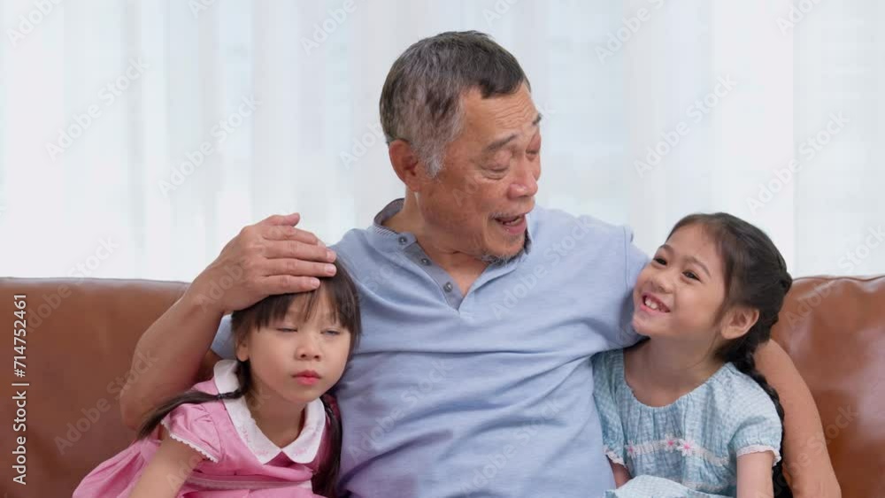 Happy Asian senior grandfather sits on a couch with his granddaughter and plays with his granddaughter in the living room at home, The Concept of family having fun in their house Happy Asian senior grandfather sits on a couch with his granddaughter and plays with his granddaughter in the living room at home, The Concept of family having fun in their house