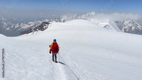 Descending from Kazbek (Kazbegi) summit 5054m rope team dressed mountaineering clothes, boots with crampons ascending by snowy slope with blue sky background and bright sun. Caucasus mountains. 4K photo