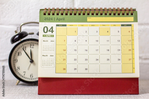 Desk calendar for April 2024 and a clock on the table. photo