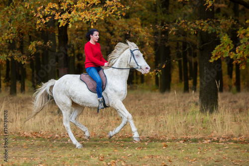 A pretty young woman and a white horse galloping around forest