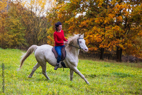 A pretty young woman and a white horse galloping through meadow
