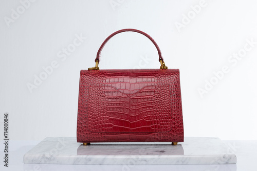 Red color, luxury fashion handbag made of crocodile skin, on marble and white background