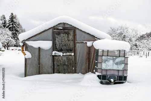garden in winter, greenhouse covered with snow, trees, garden house and garden accessories