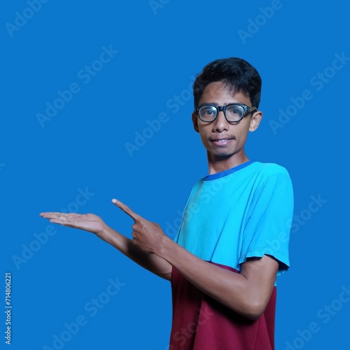 Excited Asian man wearing blue t-shirt pointing at copy space on the side  isolated on blue background.