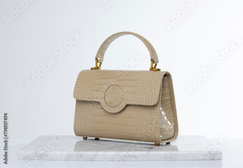 Luxury women's bag made of beige leather, on a marble floor and white background in the studio