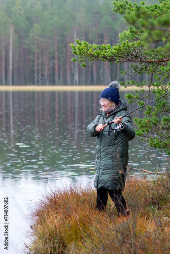 fisherwoman on the shore of a swamp lake, forest and swamp vegetation, rainy and cloudy day