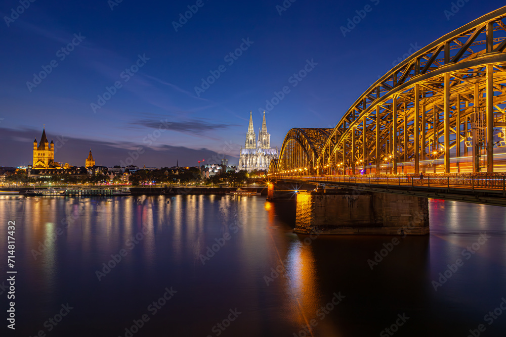Fototapeta premium Night cityscape with laminated warm light, Twilight time in the evening with Cathedral (Kölner Dom) as background, The Hohenzollern Bridge is a bridge crossing the river Rhine, Cologne city, Germany.
