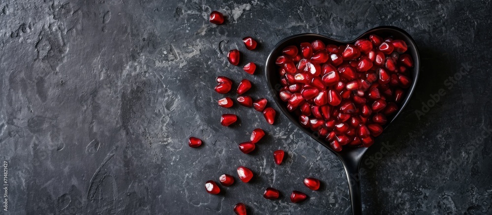 Pomegranate seeds on heart-shaped spoon, black table. Flat lay, copy space. Pomegranate seeds on heart-shaped spoon, black table. Flat lay, copy space.