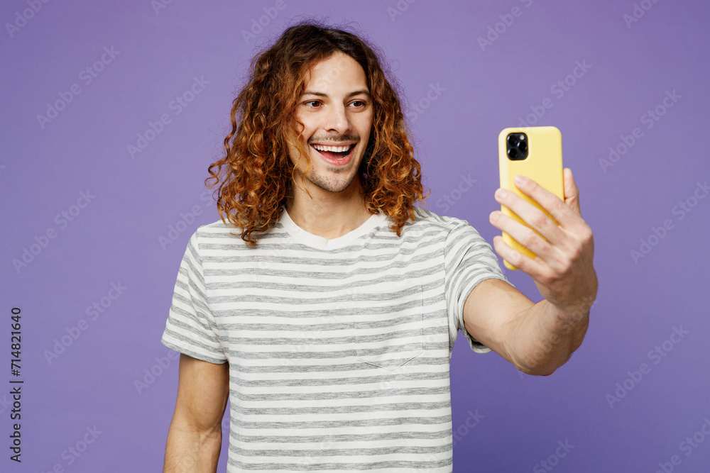 Young man wear grey striped t-shirt casual clothes doing selfie shot on mobile cell phone post photo on social network isolated on plain pastel purple background studio portrait. Lifestyle concept. Young man wear grey striped t-shirt casual clothes doing selfie shot on mobile cell phone post photo on social network isolated on plain pastel purple background studio portrait. Lifestyle concept.