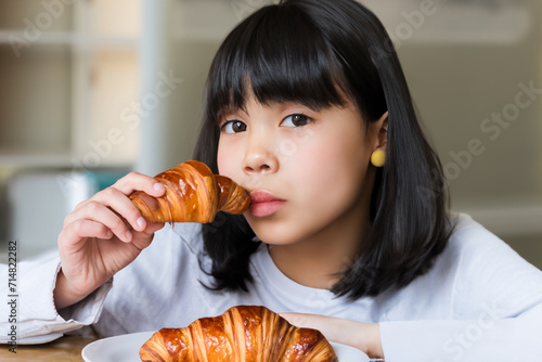 girl with a croissant. little Asian girl with short black hair and in a white jacket sits at the table and eats a croissant  food concept