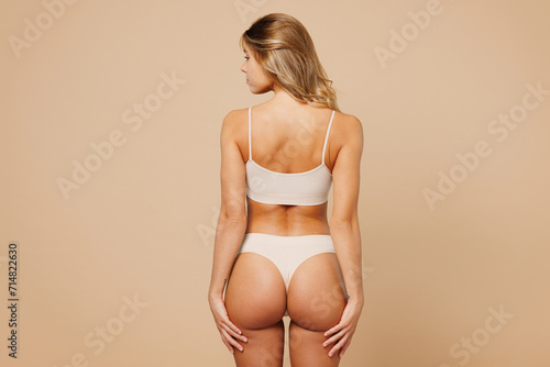 Back rear view young nice lady woman with slim body perfect skin wearing nude top bra lingerie stand hold hands on thighs isolated on plain pastel light beige background. Lifestyle diet fit concept.