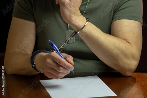 A handcuffed military man signs a document on white paper, interrogation and testimony.