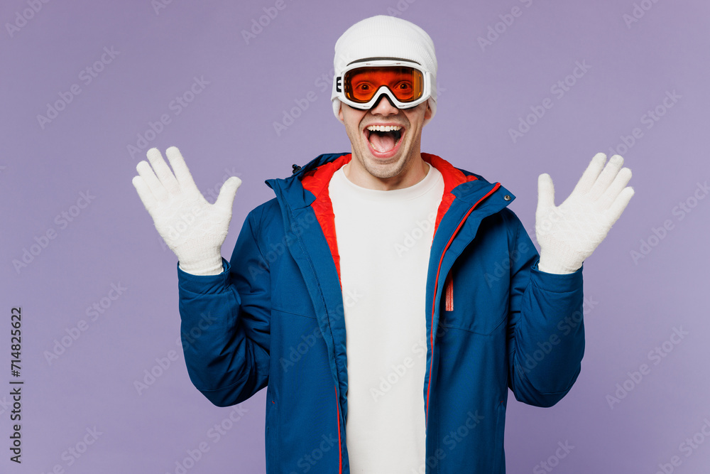 Skier surprised shocked amazed man wear warm blue windbreaker jacket ski goggles mask hat look camera spread hands spend extreme weekend winter season in mountains isolated on plain purple background. Skier surprised shocked amazed man wear warm blue windbreaker jacket ski goggles mask hat look camera spread hands spend extreme weekend winter season in mountains isolated on plain purple background.