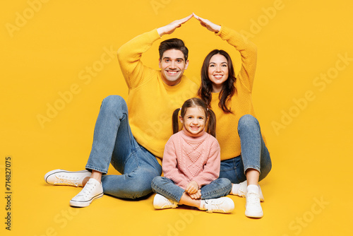 Full body young parents mom dad with child kid girl 7-8 year old wear pink sweater casual clothes hold folded hands above head like house roof isolated on plain yellow background. Family day concept. photo