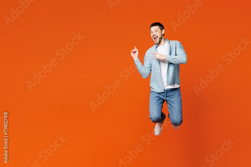 Full body young fun man he wears blue shirt white t-shirt casual clothes jump high point index finger aside on area mock up isolated on plain red orange background studio portrait. Lifestyle concept. photo