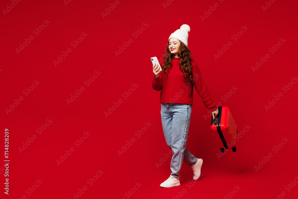 Traveler woman wear sweater hat casual clothes hold bag use mobile cell phone isolated on plain red color background. Tourist travel abroad in free time rest getaway. Air flight trip journey concept. - obrazy, fototapety, plakaty 