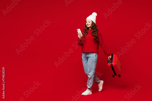 Traveler woman wear sweater hat casual clothes hold bag use mobile cell phone isolated on plain red color background. Tourist travel abroad in free time rest getaway. Air flight trip journey concept. #714828209