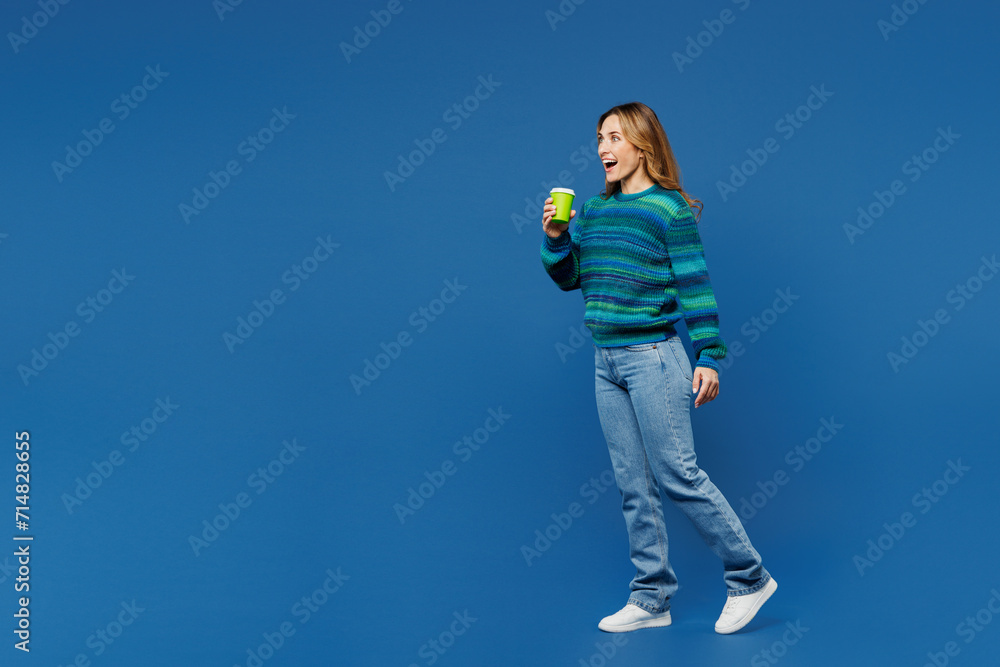 Full body young woman she wear knitted sweater casual clothes hold takeaway delivery craft paper brown cup coffee to go isolated on plain blue cyan color background studio portrait. Lifestyle concept Full body young woman she wear knitted sweater casual clothes hold takeaway delivery craft paper brown cup coffee to go isolated on plain blue cyan color background studio portrait. Lifestyle concept