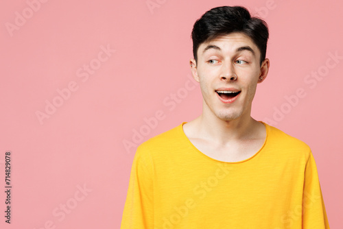 Young surprised shocked Caucasian man he wearing yellow t-shirt casual clothes look aside on area mock up isolated on plain pastel light pink color wall background studio portrait. Lifestyle concept.