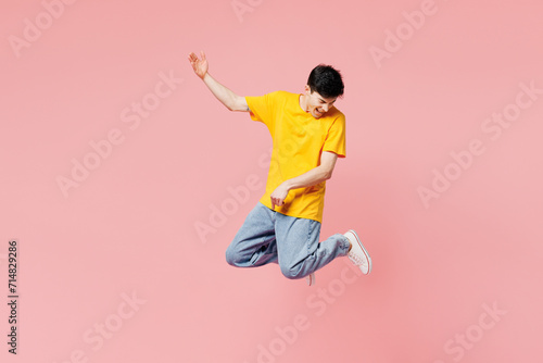 Full body expressive fun cool young man he wears yellow t-shirt casual clothes jump high play air guitar isolated on plain pastel light pink color wall background studio portrait. Lifestyle concept.